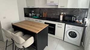A compact kitchen with a wooden dining table, two chairs, a washing machine, and a microwave. - Welcome to MBA HOUSE - Relaxation & Comfort in Guadeloupe! (Pointe-à-Pitre)