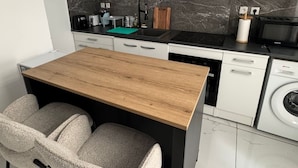 A modern kitchen with white cabinets, a black countertop, a wooden table, and two grey chairs. - Welcome to MBA HOUSE - Relaxation & Comfort in Guadeloupe! (Pointe-à-Pitre)
