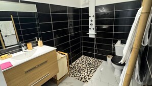 A bathroom with a black tiled shower, a white sink with a wooden vanity, and a toilet. - Welcome to MBA HOUSE - Relaxation & Comfort in Guadeloupe! (Pointe-à-Pitre)
