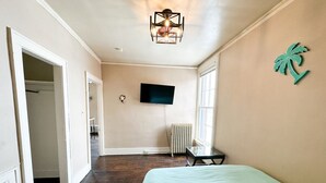 A bedroom with a bed, a TV, a radiator, and a palm tree decoration. - Downtown Historical 1 Bed Apt (Bay City)
