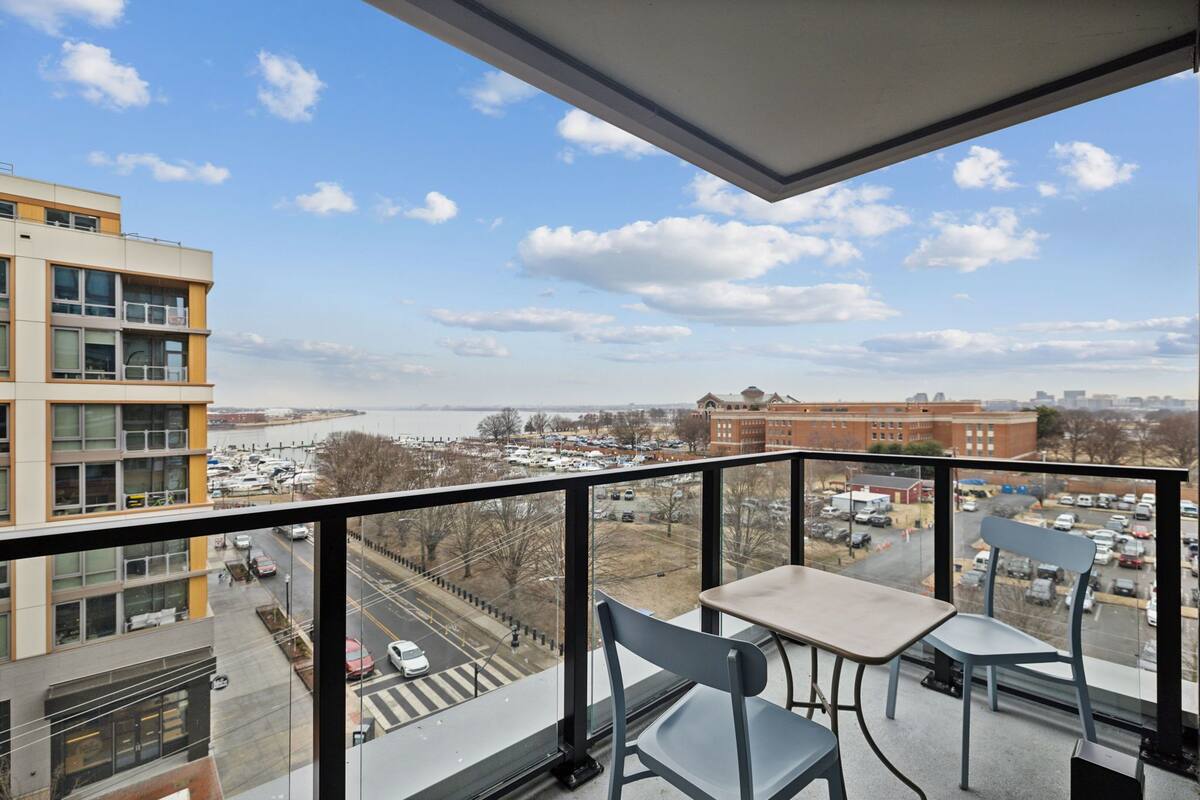 A balcony with a table and chairs, overlooking a parking lot and buildings.