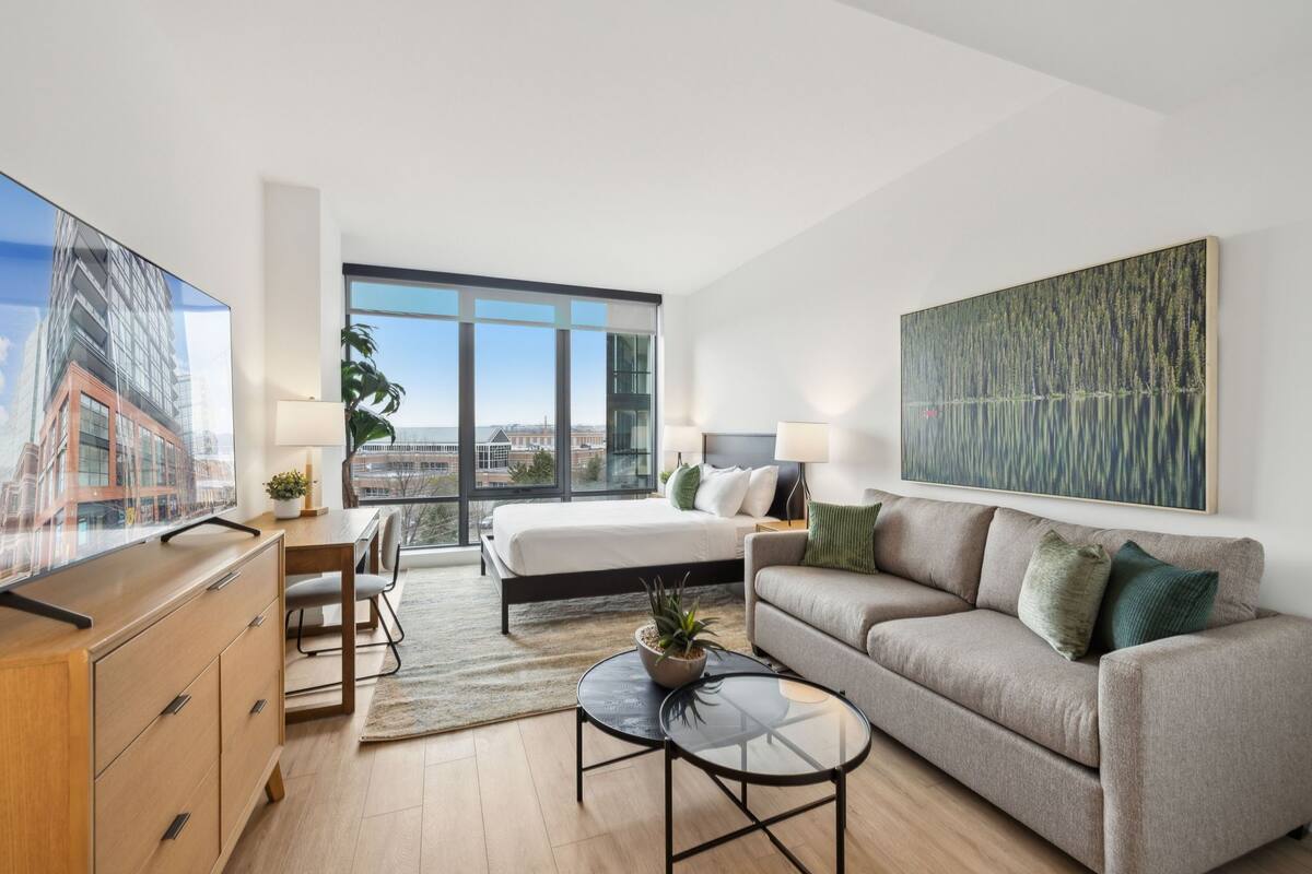 A modern hotel room with a large bed, a sofa, a desk, and a TV.