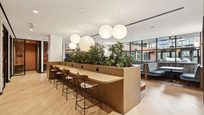 A modern interior with a wooden bar area, seating, and large windows offering views of the city. - Placemakr Buzzard Point (Washington)