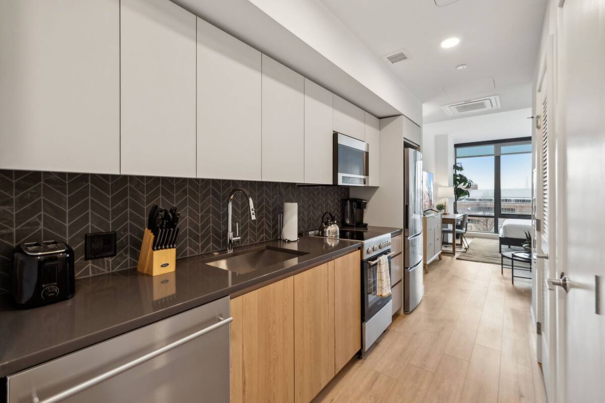 A modern kitchen with a herringbone tile backsplash, stainless steel appliances, and wooden cabinets.