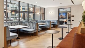 A modern restaurant interior with seating arrangements, including booths and tables, and large windows offering views of the cityscape. - Placemakr Buzzard Point (Washington)