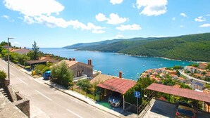 A coastal town with a clear view of the sea, a parking area, and buildings with red-tiled roofs.