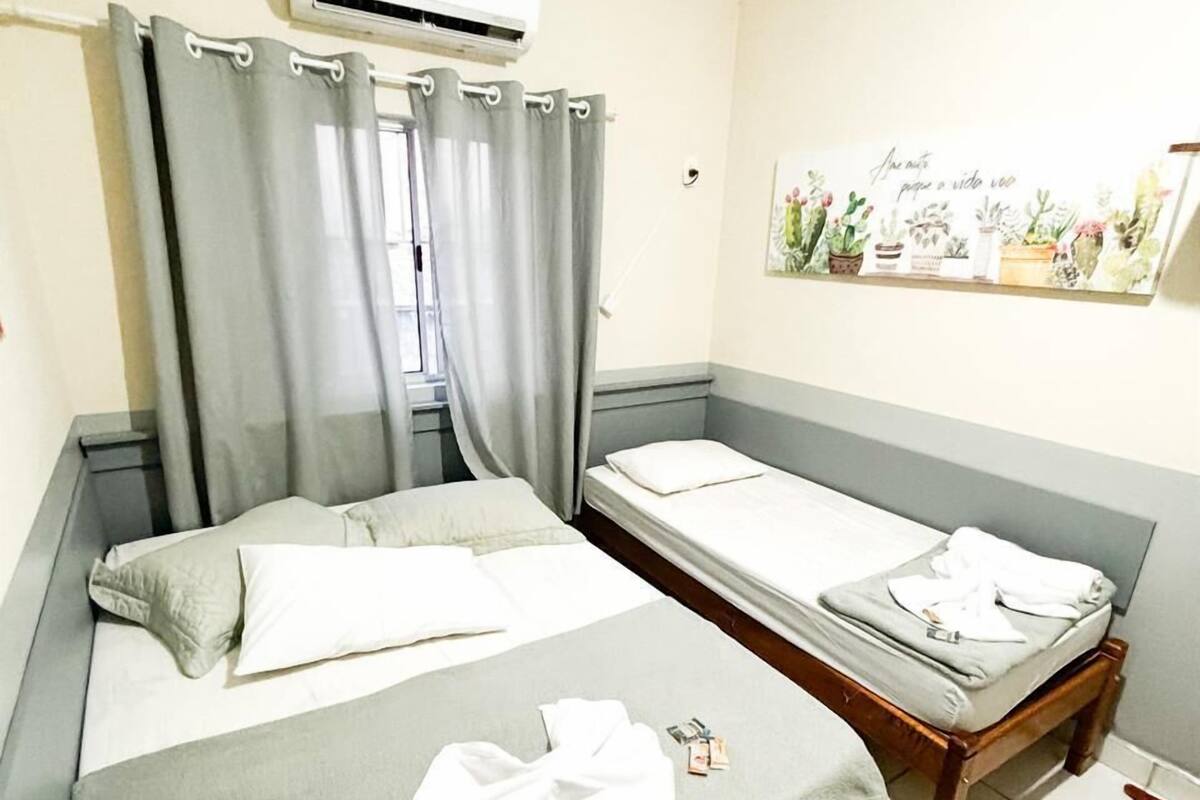 A hotel room with two beds, a grey curtain, an air conditioning unit, and a wall decoration.