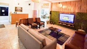 Un hall d’hôtel moderne avec un canapé, des fauteuils, un téléviseur et un comptoir d’accueil.