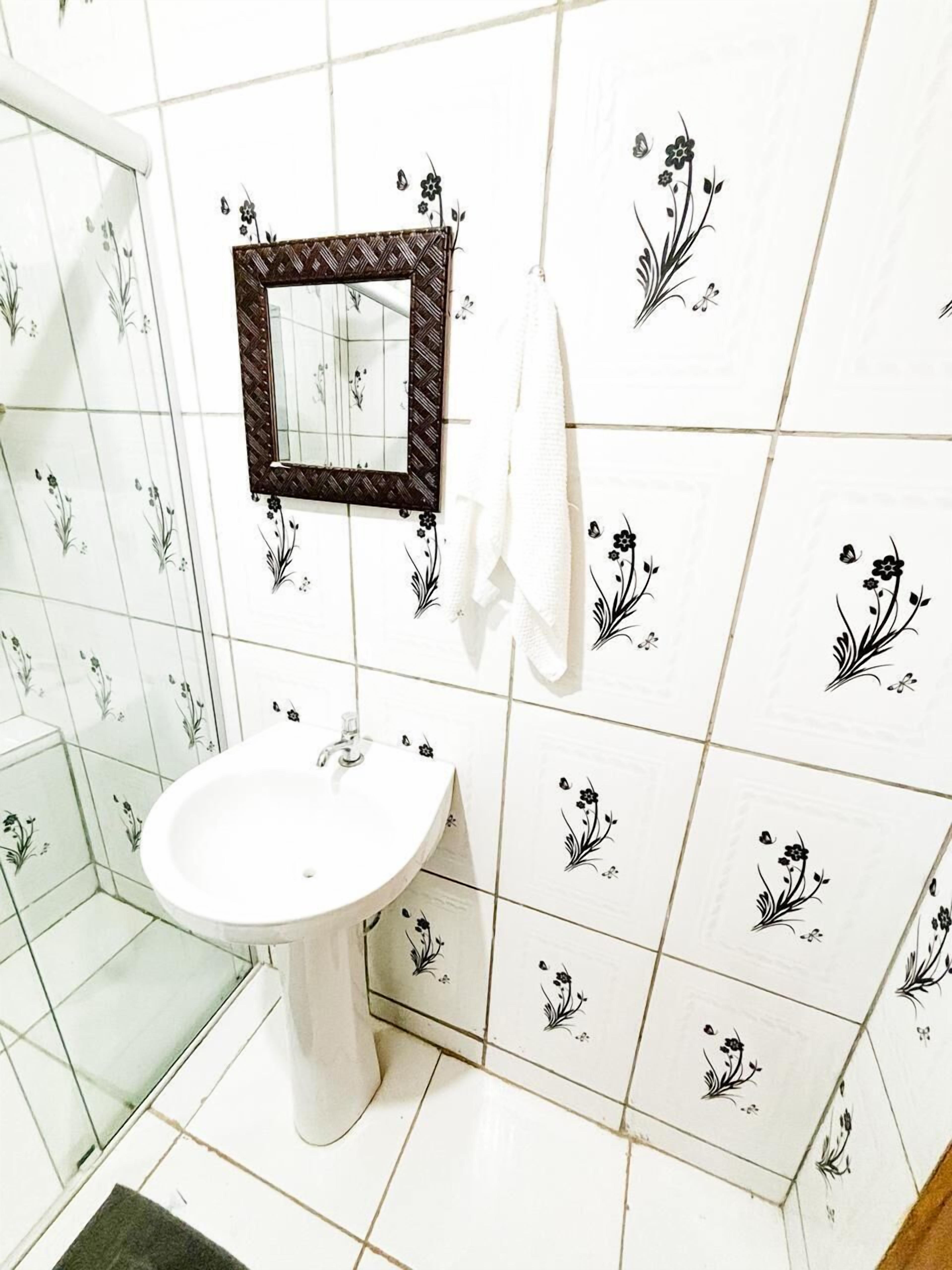 Um banheiro com pia branca, espelho com moldura de madeira e azulejos estampados com flores.