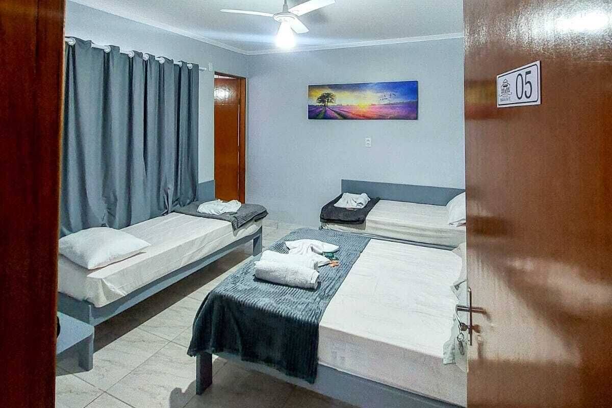 A hotel room with two single beds, a ceiling fan, a painting on the wall, and a door with a number.