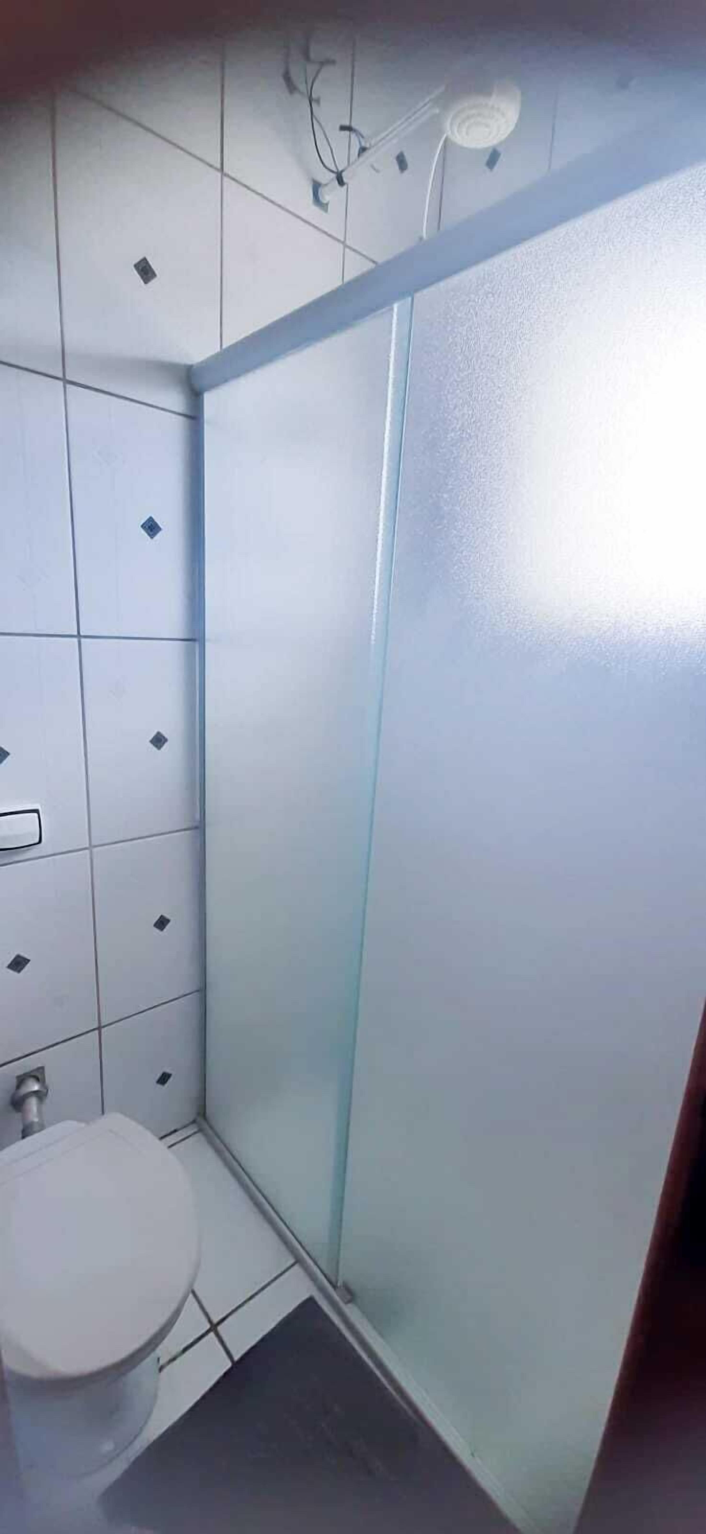 A bathroom with a toilet, a shower with frosted glass doors, and tiled walls.