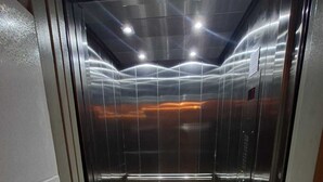 Un ascensor con paredes metálicas y piso de baldosas verdes.