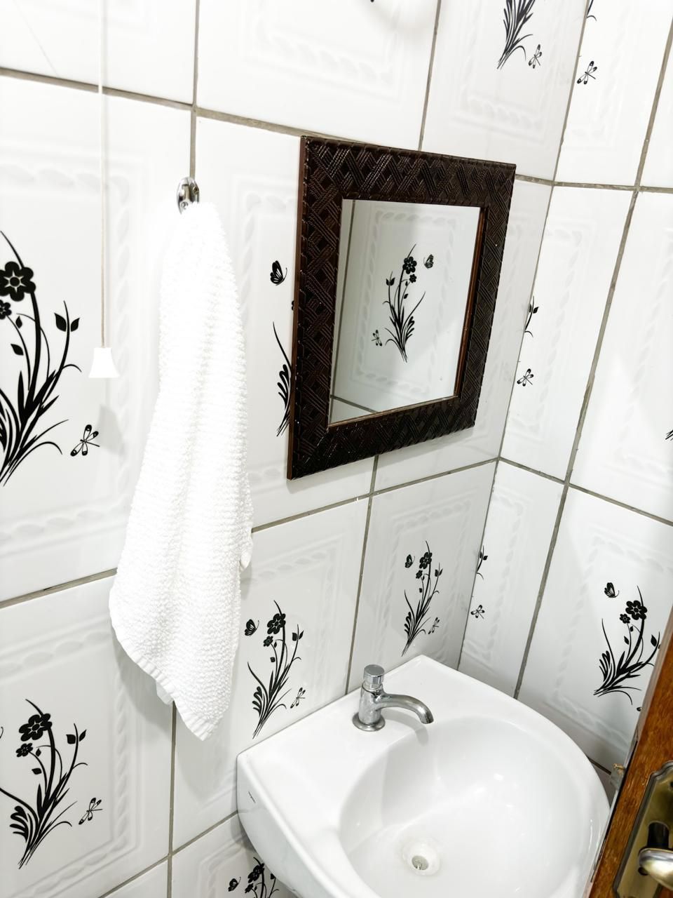 Un baño con azulejos blancos, un lavamanos blanco, un espejo y una toalla colgada en un perchero.