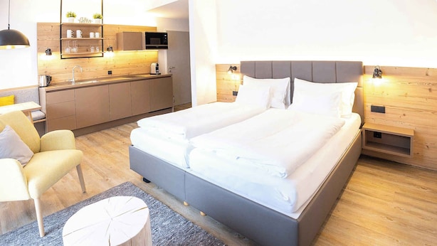 Una habitación de hotel moderna con una cama grande, un escritorio pequeño, una silla, una mesita de noche de madera y una zona de cocina con microondas.