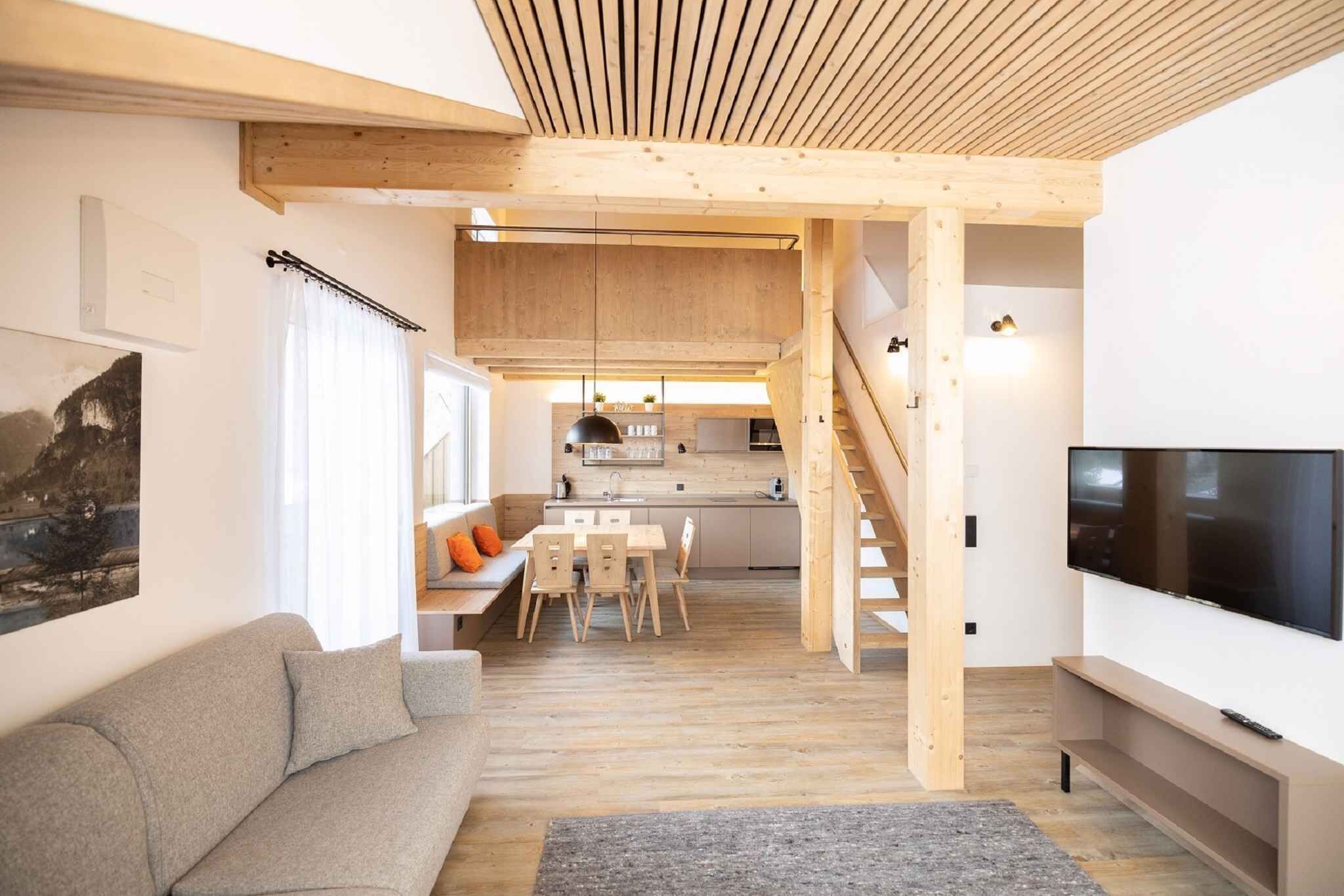 Een modern interieur met houten plafond, een bank, een eettafel, een televisie en een keukenhoek.