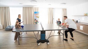 Una mesa de ping pong en una habitación con techo lleno de pequeños agujeros, cortinas y un cartel en la pared.