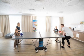 A table tennis table in a room with a ceiling with small holes, curtains, and a poster on the wall.