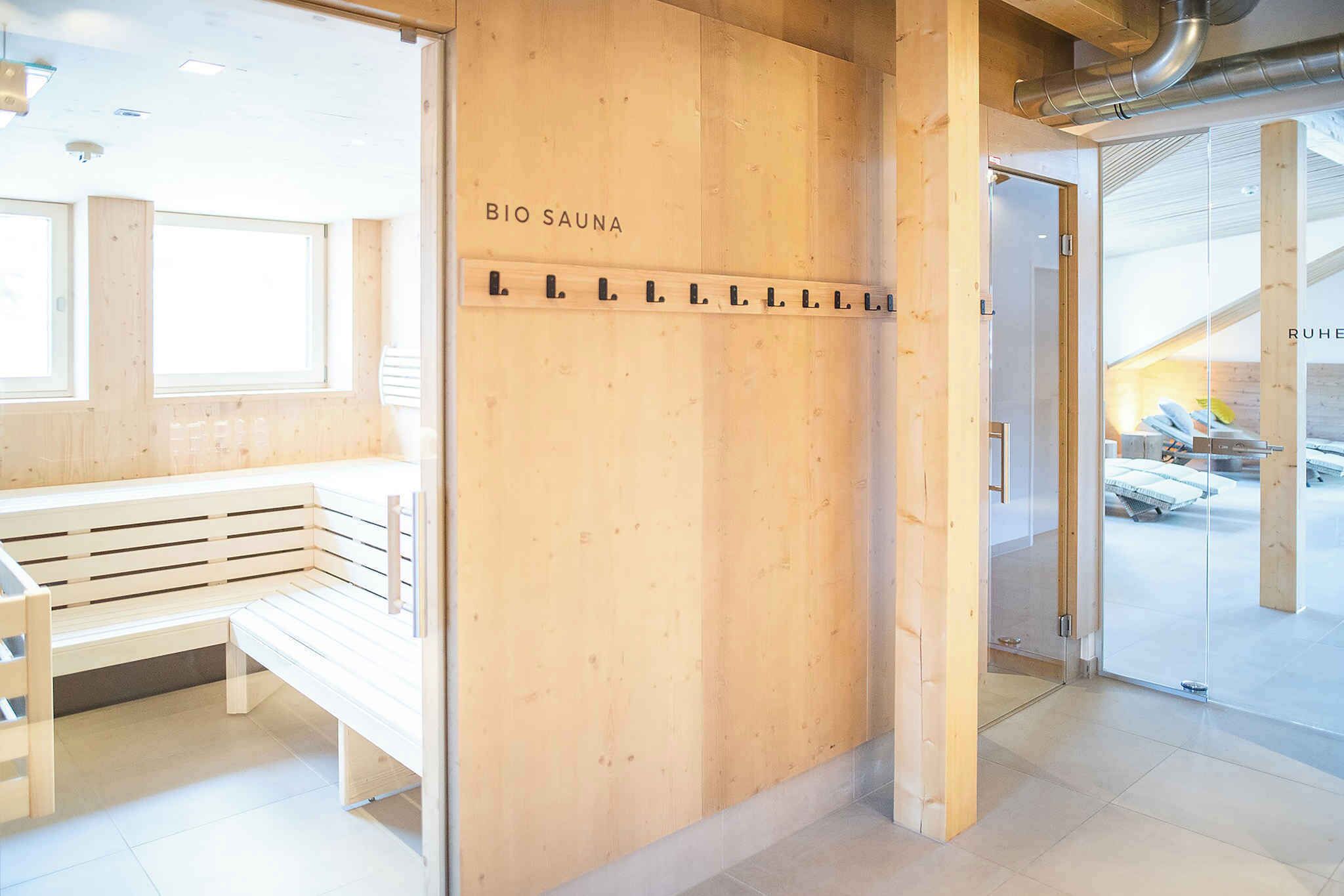 Een houten receptiebalie met 'BIO SAUNA' aanduiding, een bankje en een glazen deur naar een sauna.