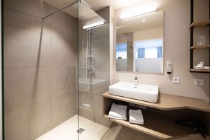 Ein modernes Badezimmer mit einer gläsernen Dusche, einem weißen Waschbecken und einem Spiegel darüber.