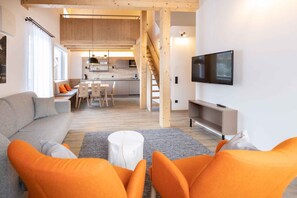 Ein modernes Wohnzimmer mit einer Couch, orangefarbenen Sesseln, einem Fernseher und einer Treppe, die zu einer oberen Ebene führt.