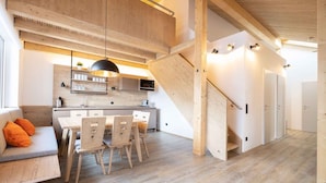 Una cocina moderna con armarios de madera, un comedor con mesa y sillas, y una escalera que sube a otro nivel.