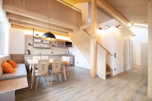 A modern kitchen with wooden cabinetry, a dining area with a table and chairs, and a staircase leading to another level.