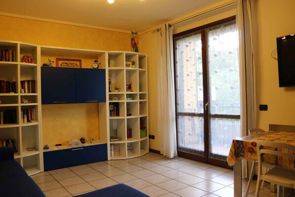 A room with a bookshelf, a table with a tablecloth, and a sliding glass door leading to an outdoor area.