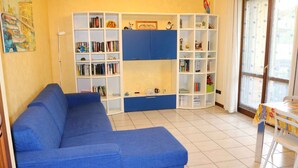 Een woonkamer met een blauwe bank, een boekenkast en een klein tafeltje met een stoel.