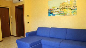Een kamer met een blauwe bank en een schilderij van een havenlandschap aan de muur.