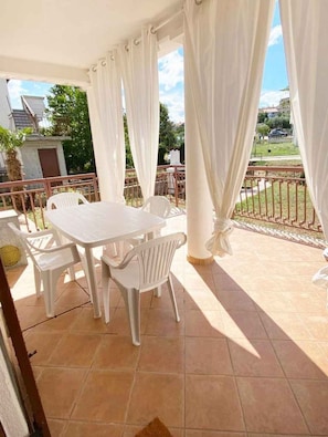 A covered patio area with a table and chairs, a railing, and a view of the surrounding landscape. - Holiday apartment with air conditioning and terrace (Funtana)