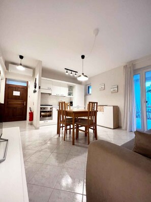 A modern kitchen with white cabinets, a dining table with chairs, a ceiling fan, and a large window with curtains. - Holiday apartment with air conditioning and terrace (Funtana)