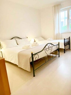 A room with two beds, a window with curtains, and a wooden floor. - Holiday apartment with air conditioning and terrace (Funtana)