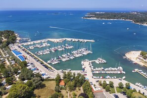 An aerial view of a marina with numerous boats docked, surrounded by greenery and a clear blue sea. - Holiday apartment with air conditioning and terrace (Funtana)