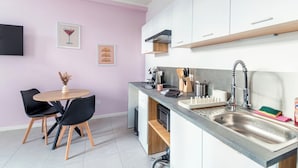 A modern kitchen with white cabinets, a stainless steel sink, and a dining area with a round table and black chairs. - Cosy, modern air-conditioned T2 (Villeurbanne)
