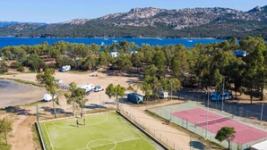 Un complexe sportif comprenant plusieurs courts de tennis, un terrain de football et un parking où sont stationnés des véhicules de loisirs.