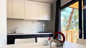Une cuisine moderne avec des meubles blancs, une bouilloire en acier inoxydable et une vue sur une terrasse en bois et des arbres.