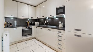 Una cocina moderna con armarios blancos, encimera negra y electrodomésticos de acero inoxidable, incluyendo un horno y un microondas.