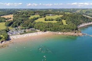 An aerial view of a coastal area with a beach, parking lot, and buildings surrounded by greenery. - 12 Rhodewood House - Near the Beach, Sea Glimpses (Saundersfoot)