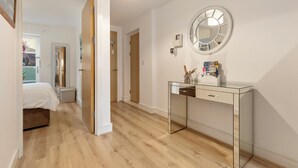 Un dormitorio moderno con suelo de madera, un escritorio de cristal y un espejo redondo en la pared.
