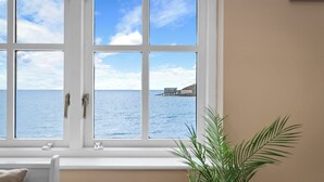 A room with a large window overlooking a body of water and a pier. - 5 Sunny Cove - Direct Beach Access, Sea Views (Tenby)