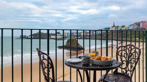 A seaside view with a table set for breakfast, overlooking the ocean and colorful buildings. - 5 Sunny Cove - Direct Beach Access, Sea Views (Tenby)