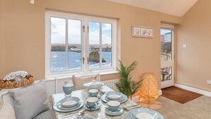 A dining area with a table set for four, a view of the sea through a window, and a door leading to an outdoor balcony. - 5 Sunny Cove - Direct Beach Access, Sea Views (Tenby)