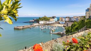 A coastal town with a marina, colorful buildings, and a prominent hilltop structure. - 5 Sunny Cove - Direct Beach Access, Sea Views (Tenby)