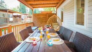 Un espace extérieur abrité, aménagé pour les repas, avec des meubles en osier, une table en bois dressée avec des assiettes, des verres et un panier de fruits.