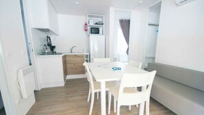 Een kleine keuken met een magnetron, spoelbak en een koelkast. Er is een eettafel met vier stoelen.