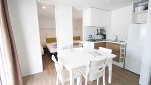 Een kleine keuken met witte kastjes, een eettafel met stoelen en een kleine koelkast.