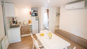 A compact kitchen with a sink, stove, and microwave, a dining area with a table and chairs, and a small seating area with a bench. - Mobilehome with air conditioning, terrace and pool (Rosolina Mare)