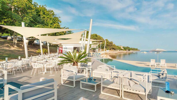 A poolside area with white lounge chairs and umbrellas, overlooking a calm body of water and a hilly landscape. - Mobile home with air conditioning, terrace and pool (Tar/Poreč)