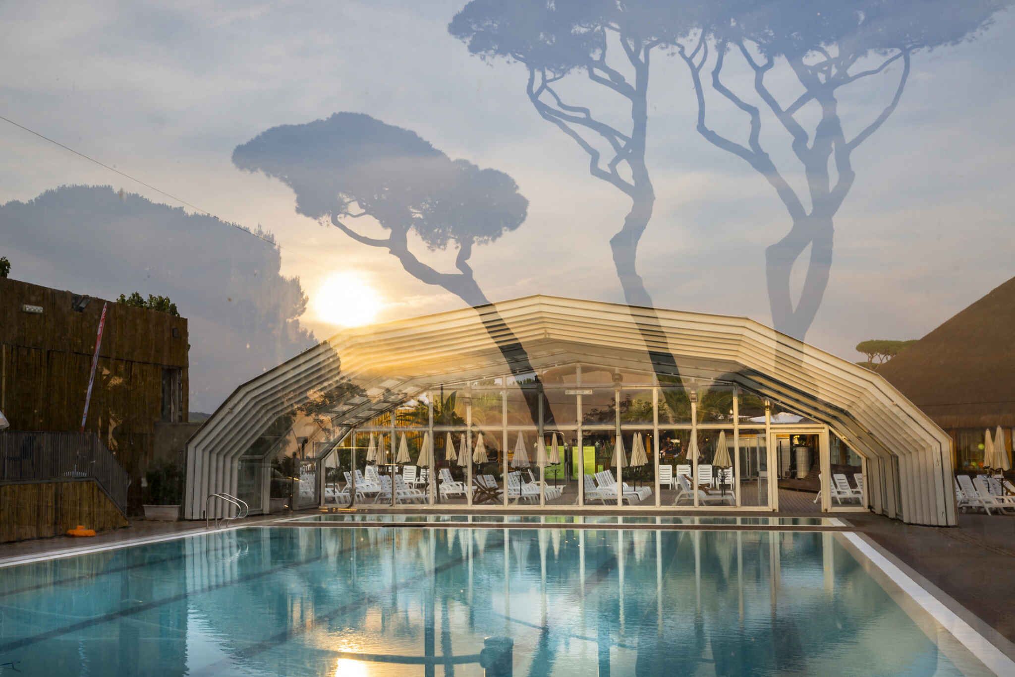 A swimming pool with lounge chairs and umbrellas, surrounded by a modern building with large windows and a curved roof.