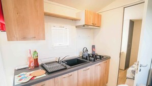 A compact kitchenette with wooden cabinets, a black countertop, a kettle, and a coffee maker. - Mobilehome with air conditioning, terrace and pool (Sami)
